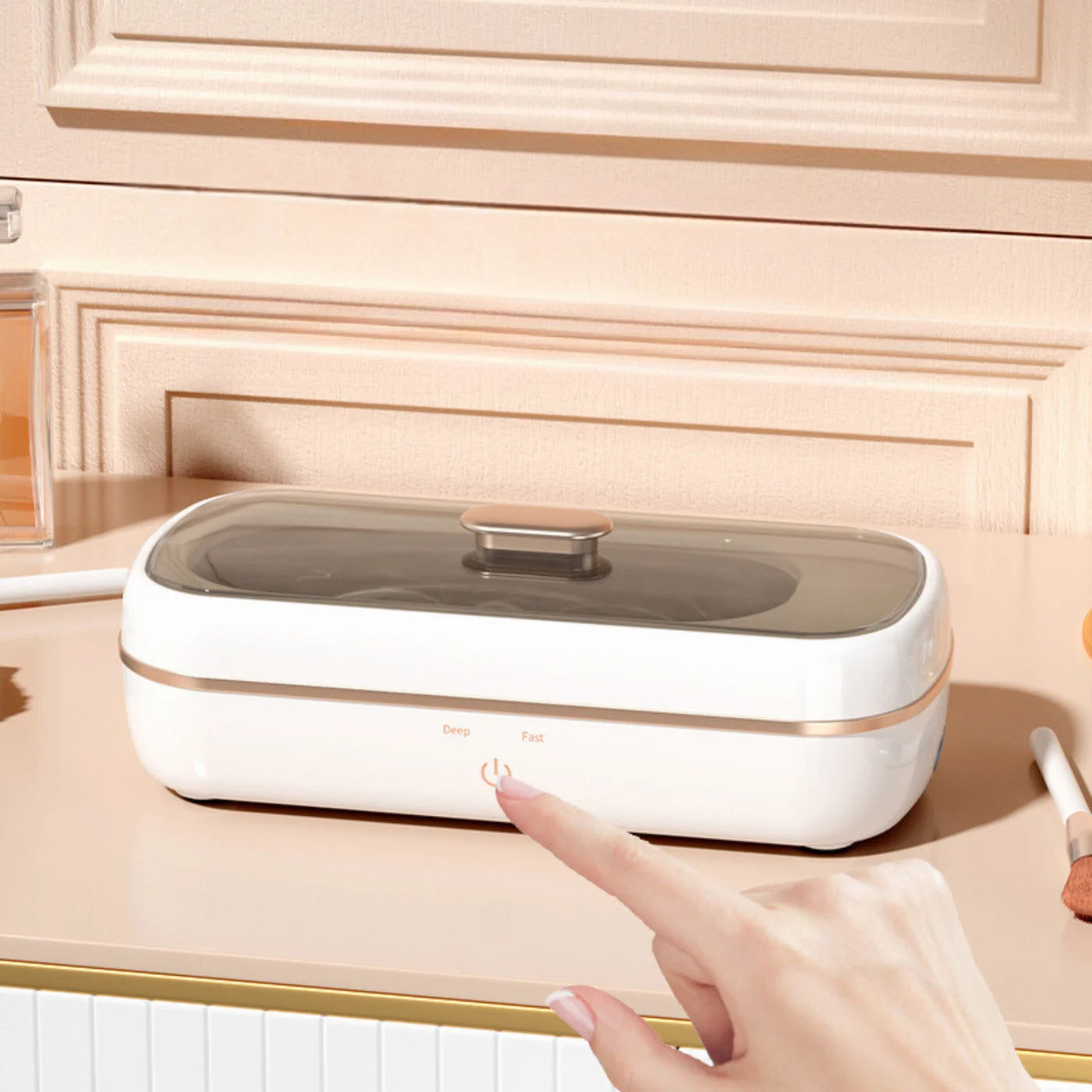 A hand touching the control button on the Shinevo ultrasonic cleaner placed on a dressing table with makeup items nearby.